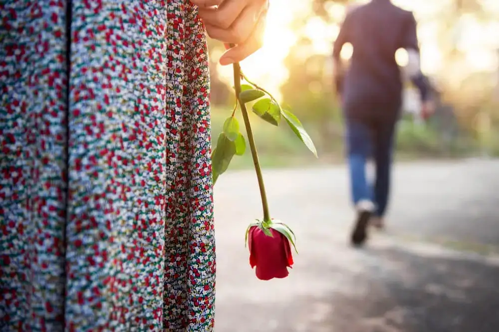 A girl standing with rose in hand and the boy is leaving as of Breakup Shayari In English - Theshayarihub.com